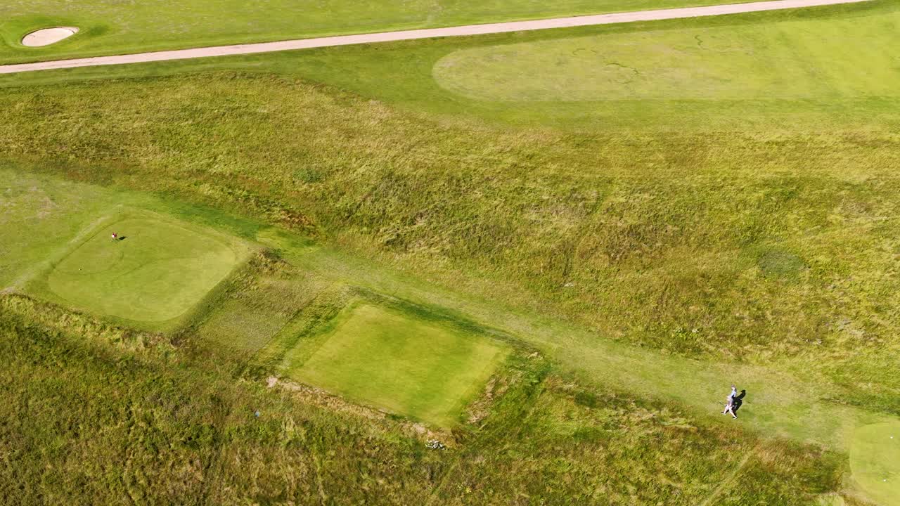 Drone captures golfers playing on green fairway in sunny, open Scottish Highlands landscape