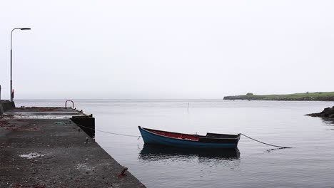 wooden boat tied to pier on a calm ocean foggy day in the faroe islands