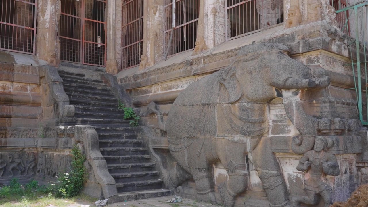 Muro de un antiguo templo hindú del sur de la India con una enorme escultura de elefante tallada en granito, flanqueado por escalones de piedra, intrincadas tallas en relieve, fachada desgastada, arquitectura patrimonial, Tamil Nadu.