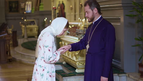 una mujer besando la mano del sacerdote.