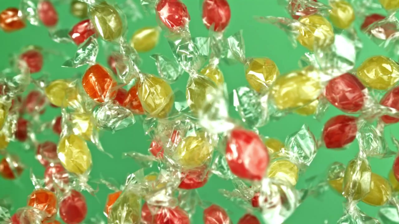 Caramelle colorate incartate che galleggiano su uno sfondo verde al rallentatore