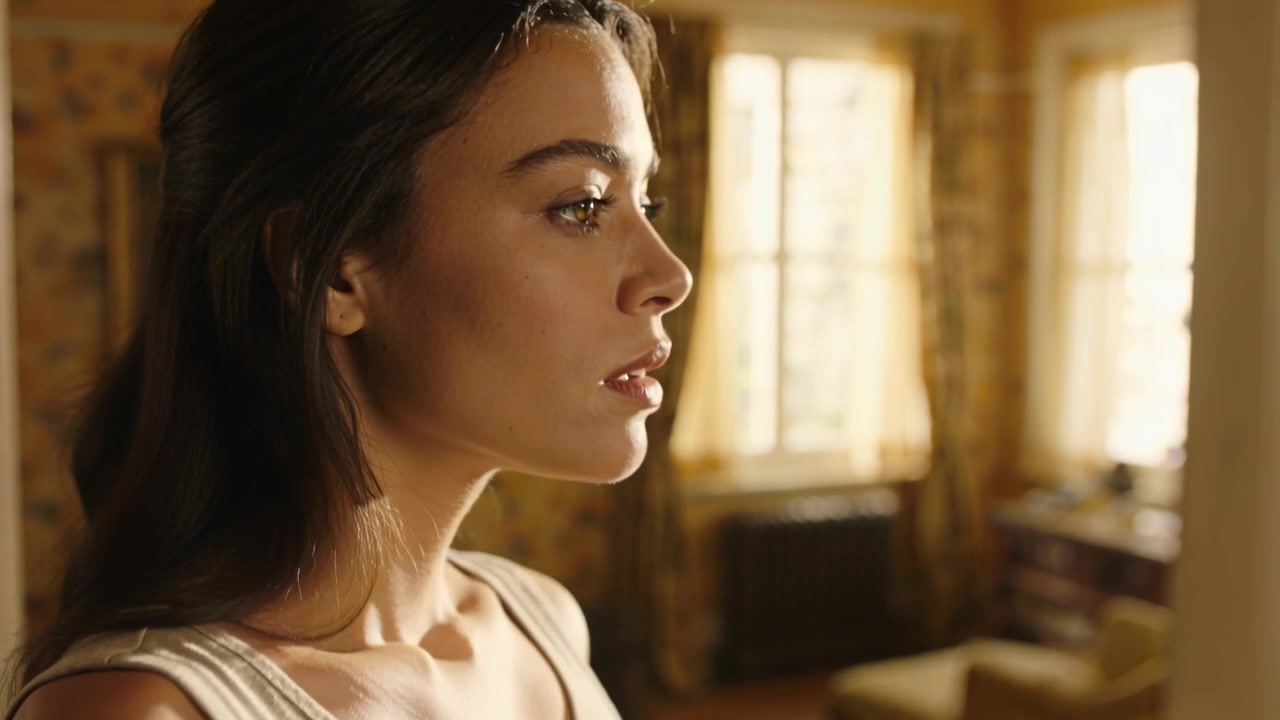 Camera pulling back woman in tank adjusting pose tucking hair gazing at light, windows, copy space