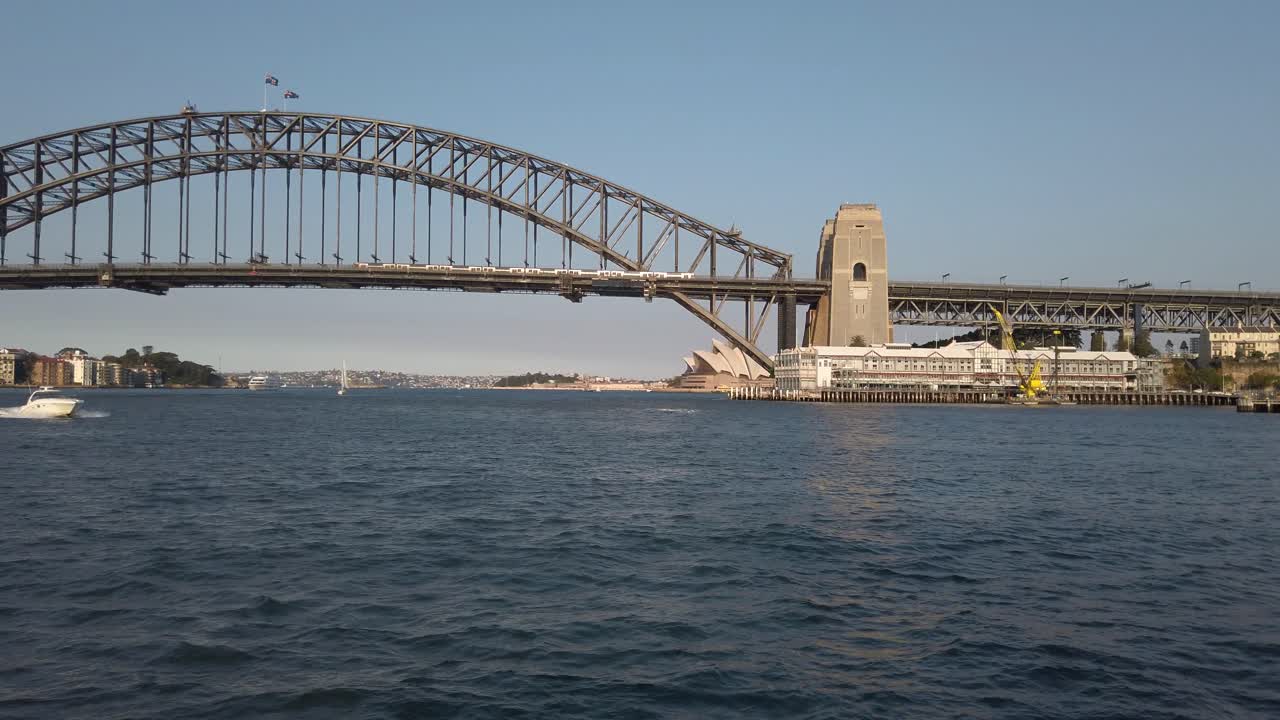 배는 호주 시드니의 일몰에 항구 다리에서 멀리 항해합니다.
