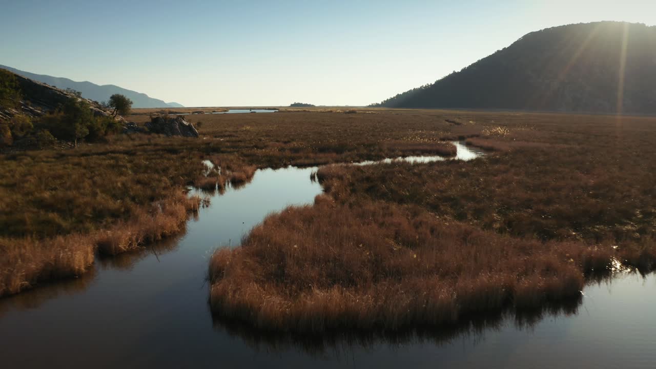 4k, High Quality, Drone flies over blue lake with dried grass covering most of the surface, leaving the lake in trail-like shapes