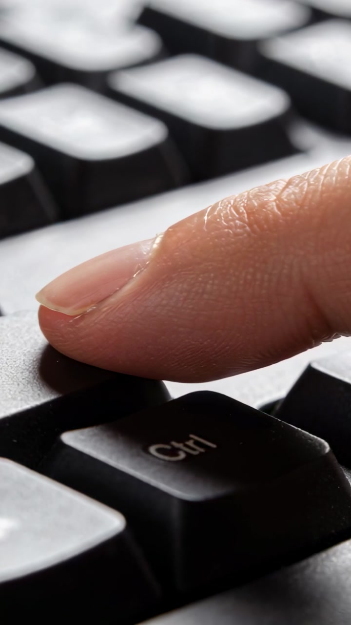Vertical video: Hovering fingertip lowering onto Ctrl key at desk, depressing black keycap gently