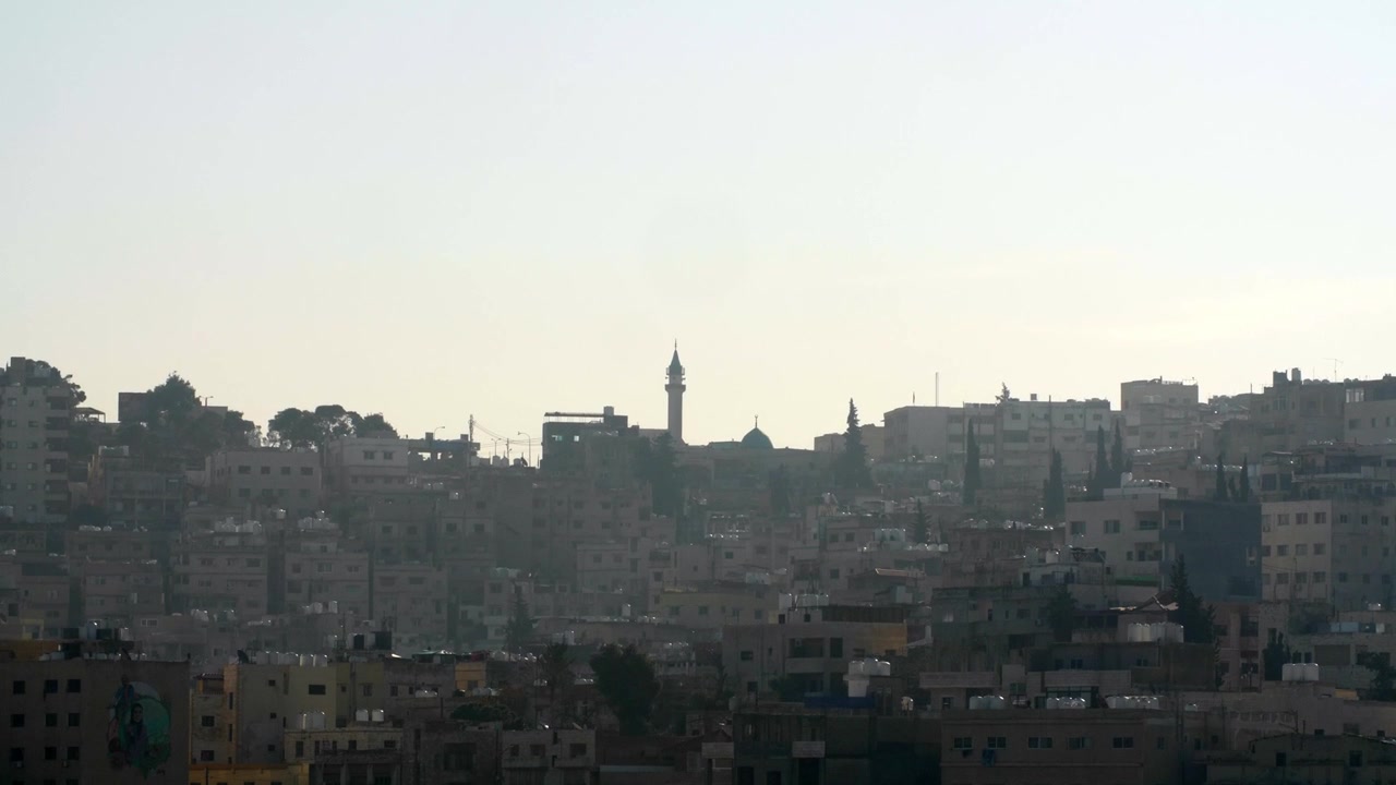 Ampia prospettiva della silhouette degli edifici della città di Amman durante una foschia nebbiosa al tramonto. Architettura urbana, dolci colline e strutture di quartieri tradizionali nella capitale della Giordania.