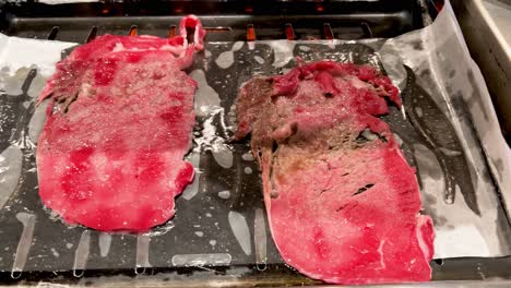 primer plano de dos filetes delgados de carne de res chisporroteando en la parrilla