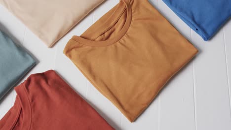 video of flat lay of multi coloured t shirts with copy space on white background