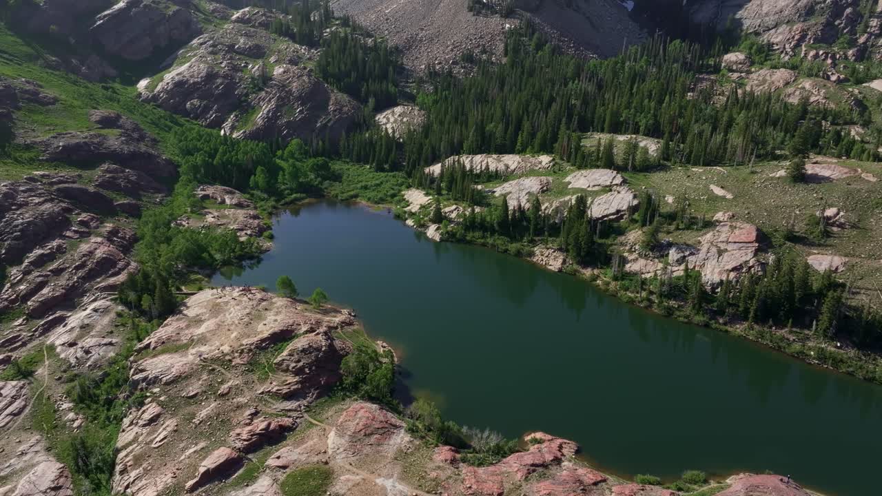 Aerial drone trucking right shot of the popular Lake Blanche in Big Cottonwood Canyon near Salt Lake City, Utah, on a bright green summer morning surrounded by rocks and lush foliage