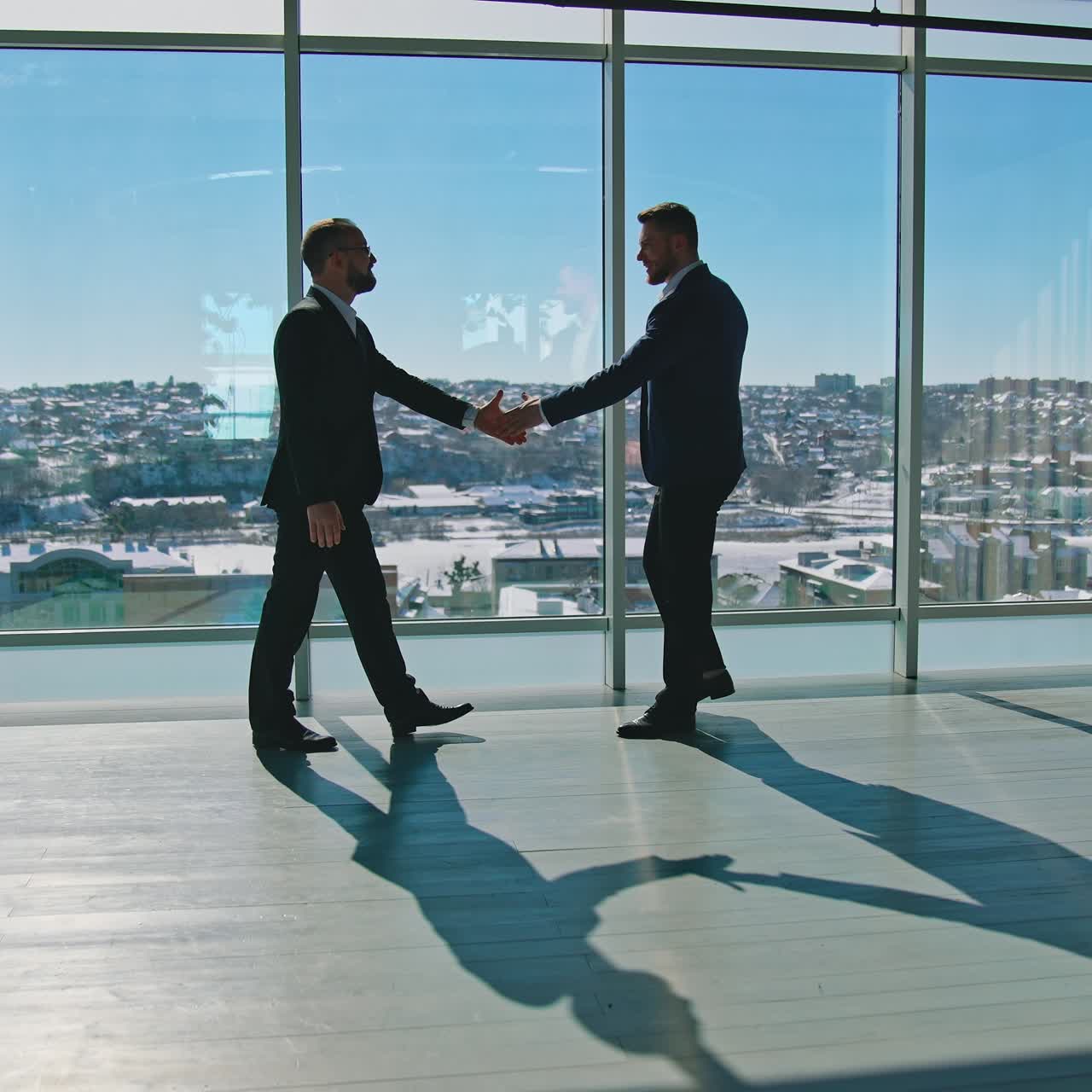 Meeting of businessmen indoors. Entrepreneurs in suits shaking hands in light office room against large panoramic windows with city view