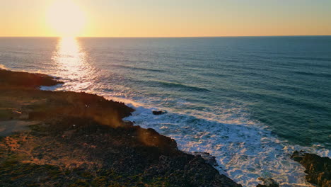 amazing sunset rocky coast with foamy ocean waves. aerial sundown over sea water