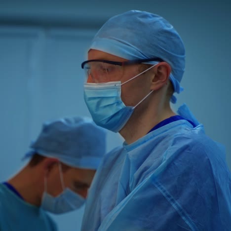 surgeon in the operating room. side view of a medical specialist in blue uniform wearing glasses. medicine concept.