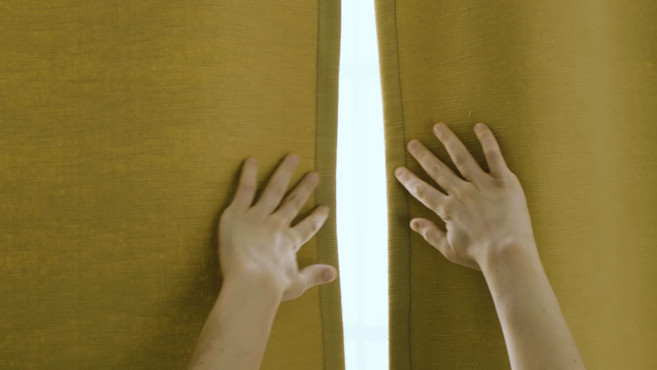두 손이 창을 덮고 있는 황토색 커튼을 천천히 열면 여과되고 섬세한 빛이 들어옵니다.