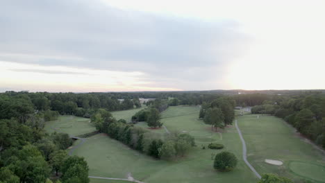 aerial drone reveals golf course during sunset, trees, forest, golfing