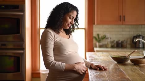 a pregnant woman gently touches her baby bump while standing in a cozy kitchen. natural light fills the space, creating a warm and intimate atmosphere as she enjoys this special time.