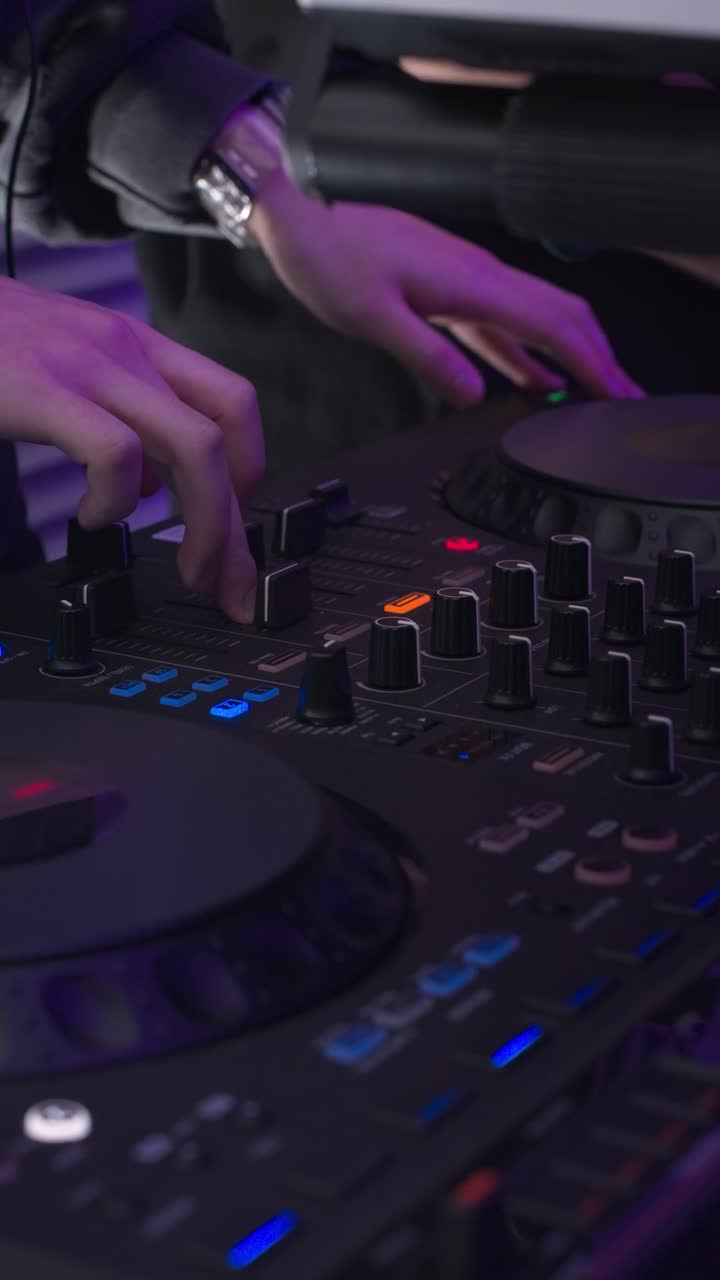 A close-up shot captures the hands of a DJ actively mixing music on a professional turntable controller, scratching a record and adjusting levels during a vibrant party or nightclub event.