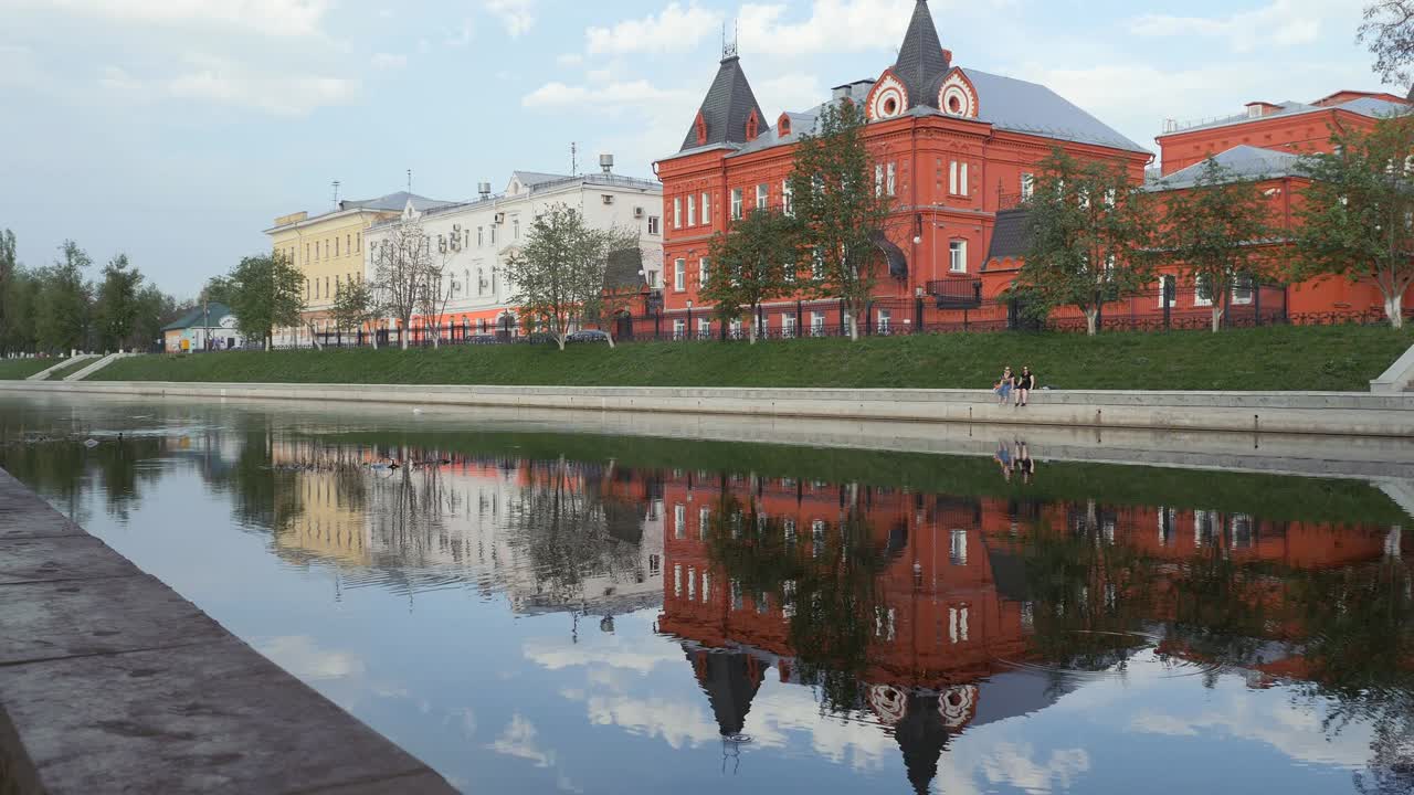 el muelle de la ciudad en la primavera. simetría en el reflejo de los edificios y las personas en el río. el edificio tiene la forma de un castillo de un ladrillo rojo