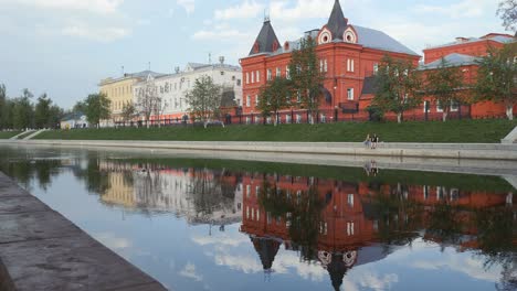 city quay in the spring. symmetry in the reflection of buildings and people in the river. the building is in the form of a castle from a red brick