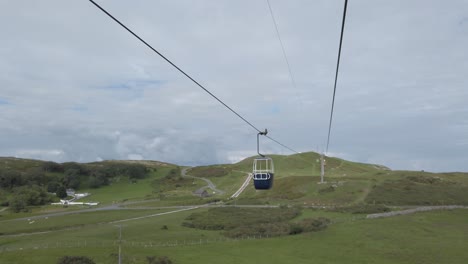 Colourful-cable-car-gondola-tourism-sightseeing-transportation-heading-up-scenic-mountain-valley-hillside