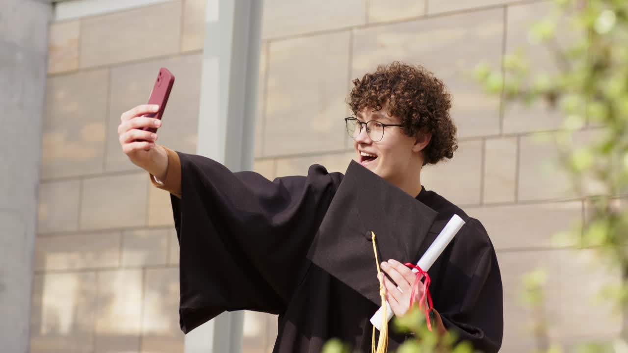 Dopo la laurea, neolaureato che tiene tocco e diploma scatta un selfie con il telefono nel campus