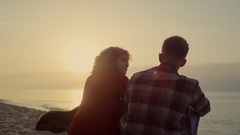 couple relaxing together on beach at sunrise. woman taking photo of sunset