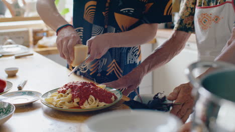 man grating cheese over freshly cooked pasta as helping grandma in kitchen