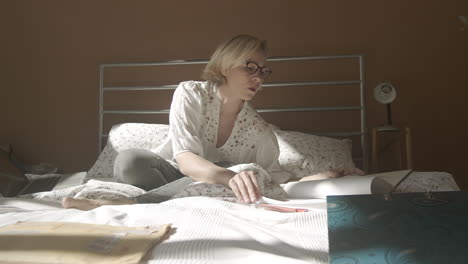 Woman-sits-with-crossed-legs-on-bed-working-at-home,-pan