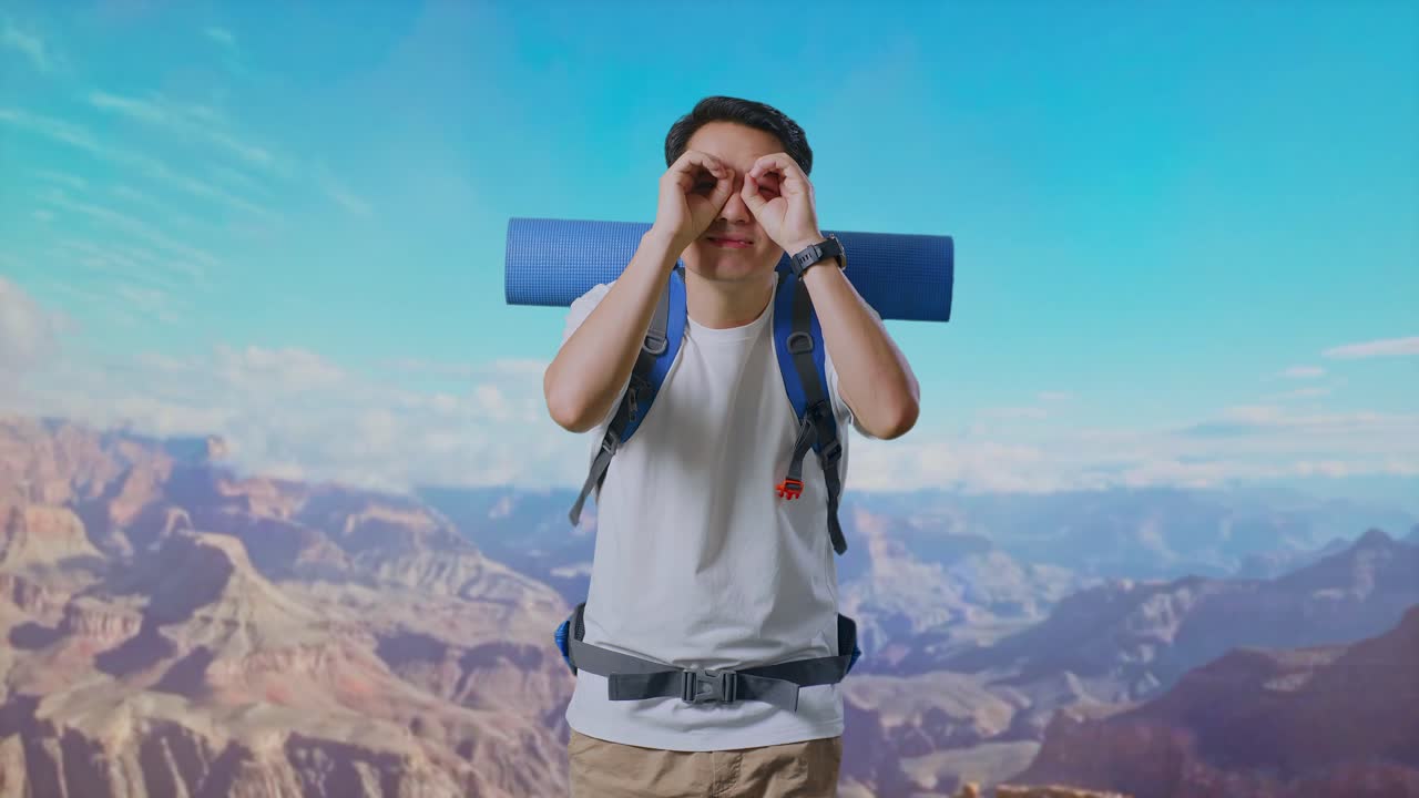Asian Male Hiker With Mountaineering Backpack Smiling And Making Binoculars Gesture Then Looking Around While Traveling At The Top Of Mountain