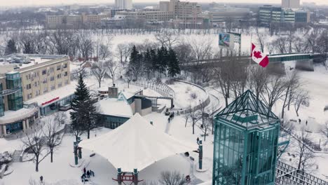 Panorámica-Aérea-Alrededor-De-La-Bandera-Canadiense-En-El-Centro-De-Winnipeg-En-Invierno