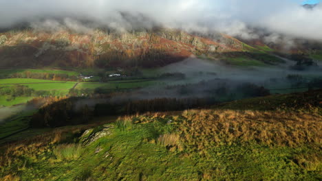 Mountains-shrouded-in-sunlit-cloud-with-flight-towards-over-sunny-green-hillock-revealing-dark-valley