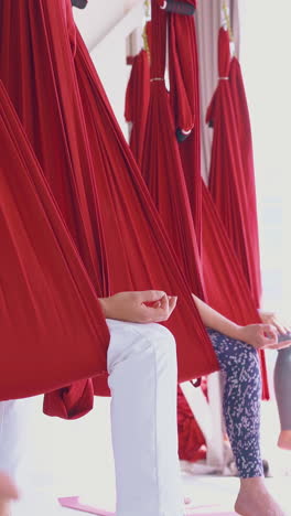 ladies sit in oriental fly yoga hammocks holding fingers in mudra position and improving mental health closeup