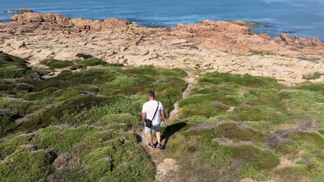 rear view of a man walking on the rocky headland to the sea in camarinas