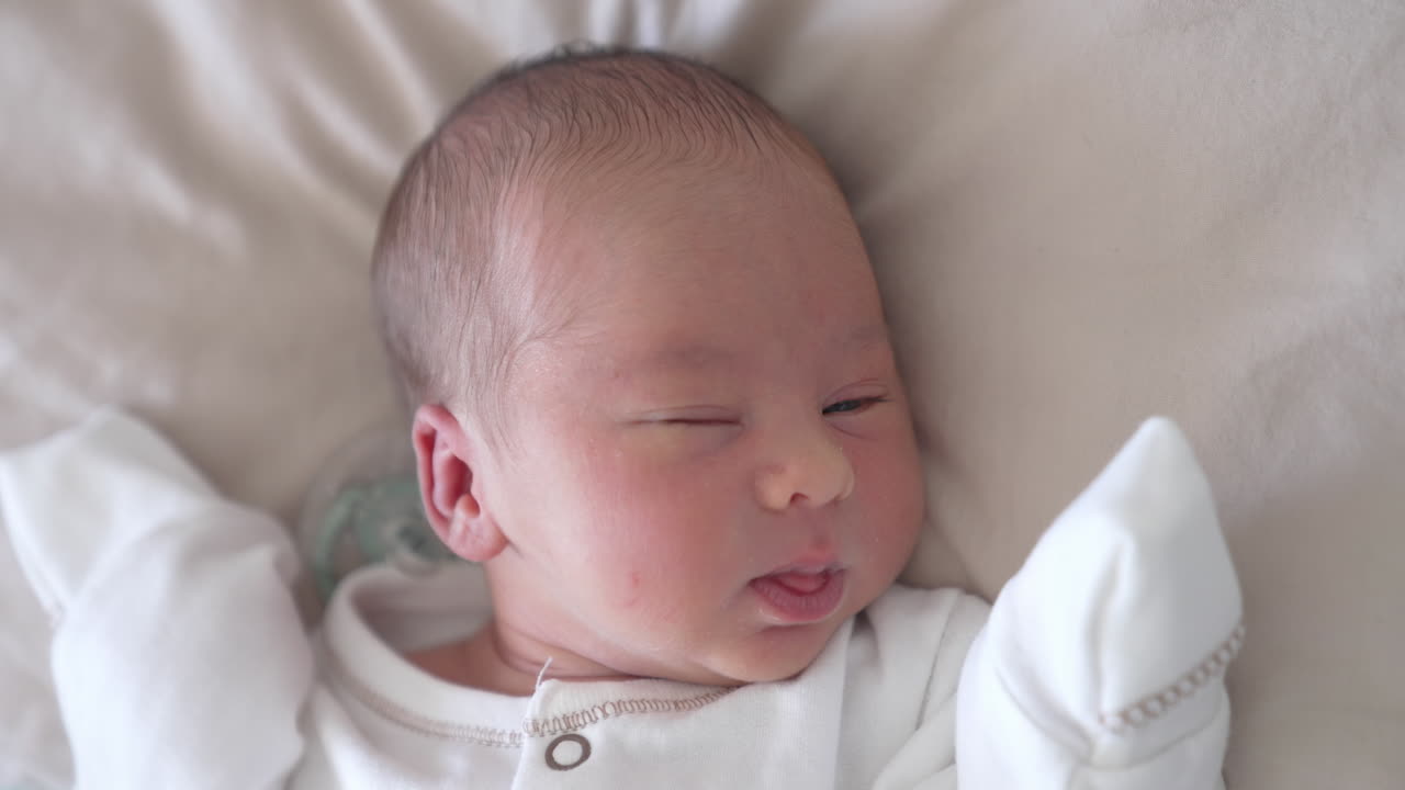 Close up view of small cute baby in light cloth. Beautiful little newborn laying on white blanket.