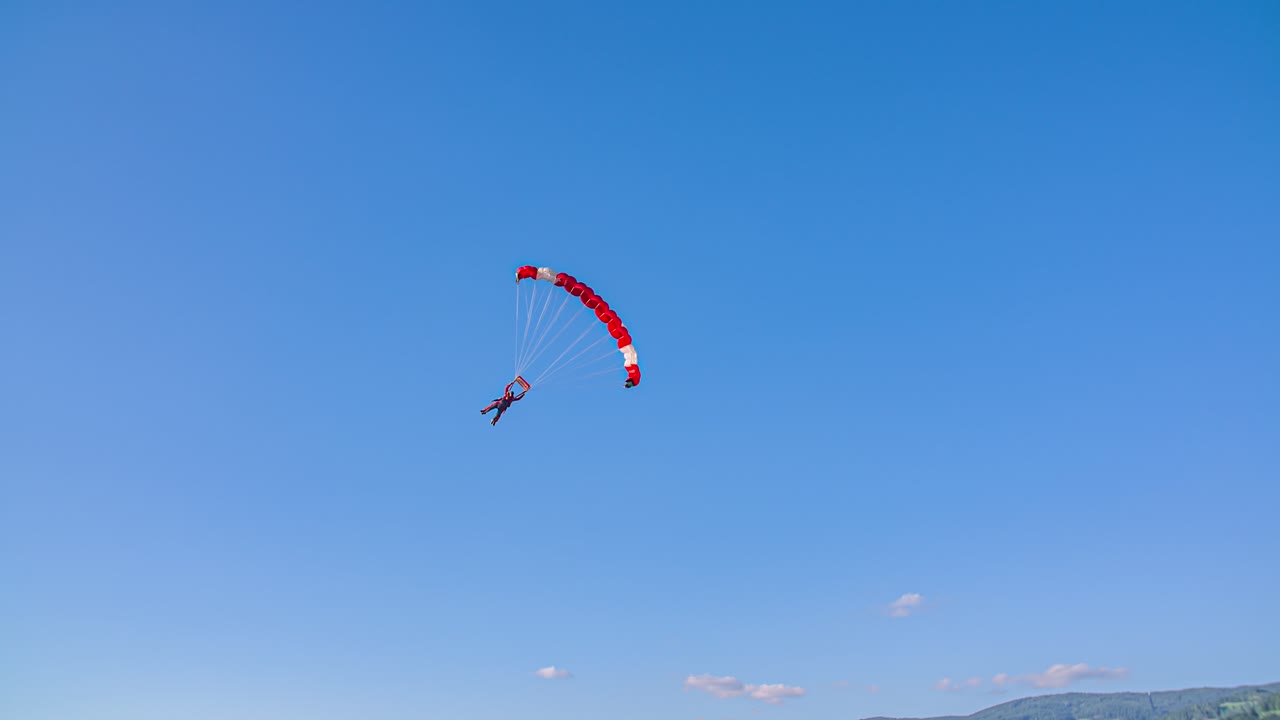 Paraglider with red wing approaching and preparing for landing on grass field