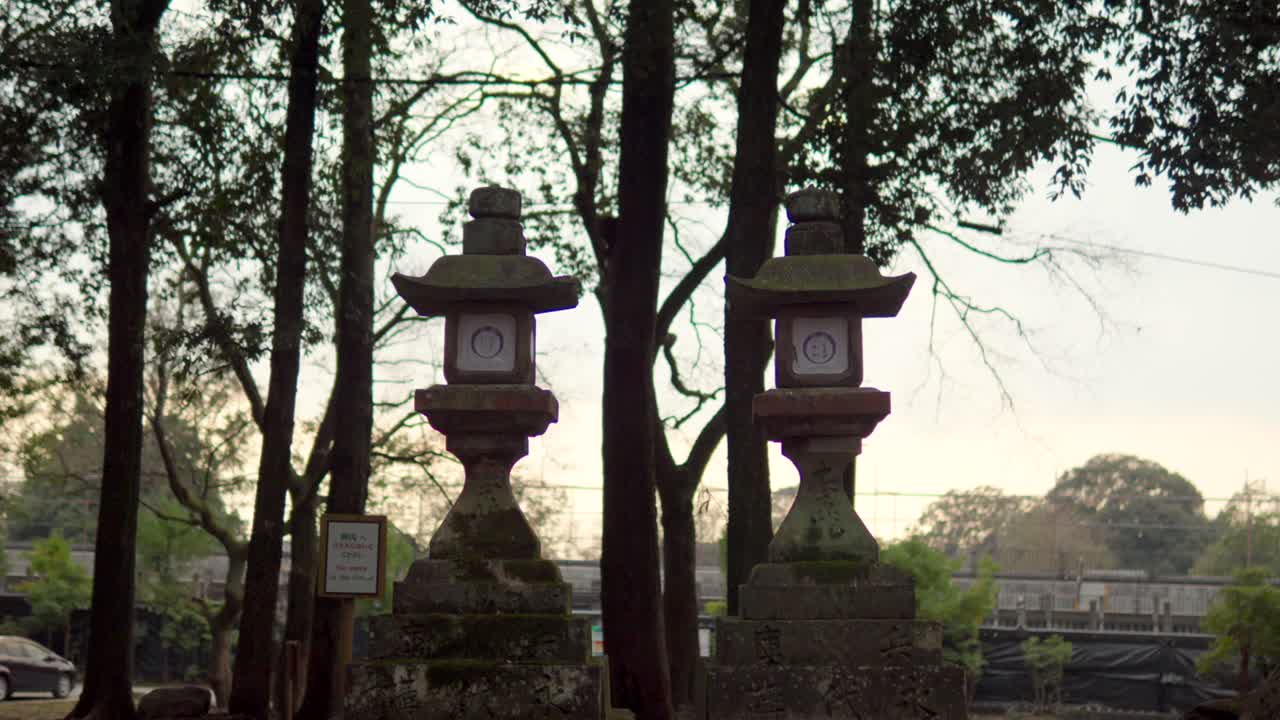 Una ripresa in tilt-down che rivela lanterne di pietra coperte di muschio su un sentiero di ghiaia durante un tramonto invernale al Santuario Kasuga Taisha a Nara, Giappone. La scena cattura l'atmosfera serena e antica del sacro