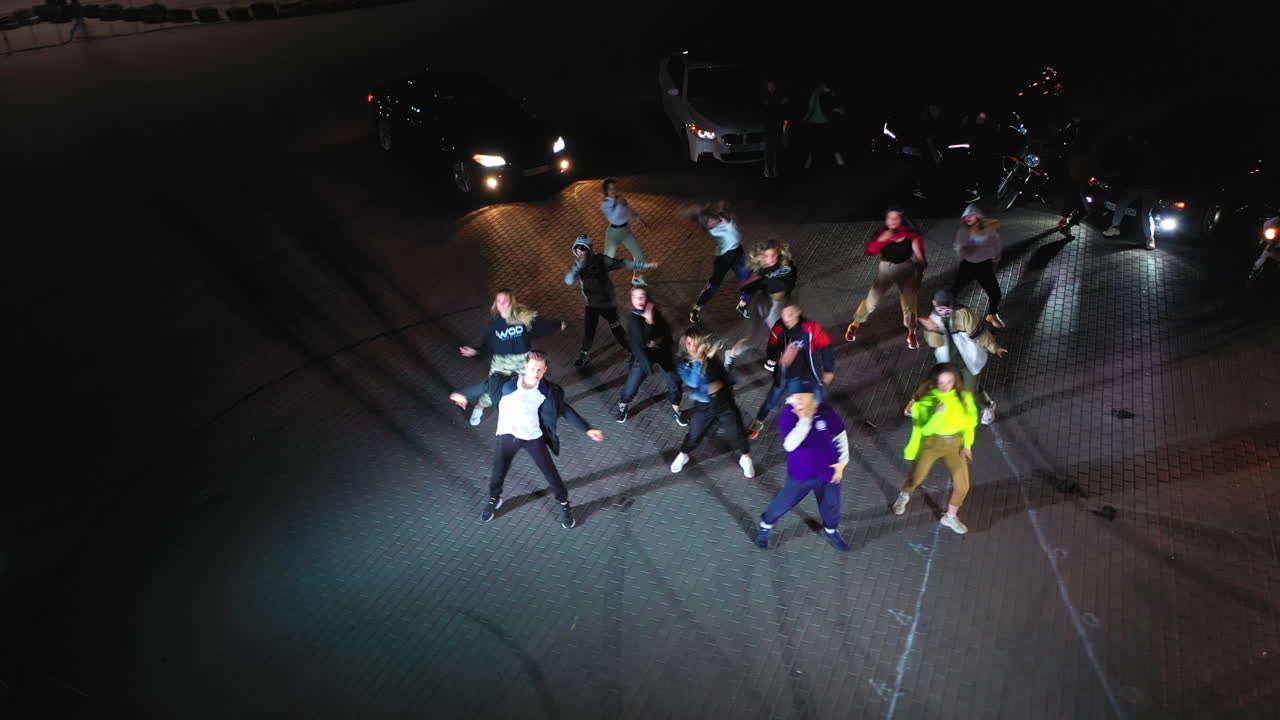 Sportive happy teenage people dance hip hop. Band dancing in flashlights. Race cars at backdrop. Top view.