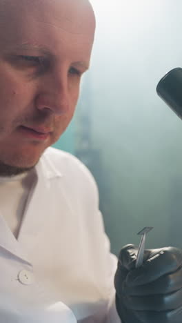 una vista de cerca de un técnico enfocado en una bata de laboratorio examinando un pequeño componente electrónico bajo un microscopio