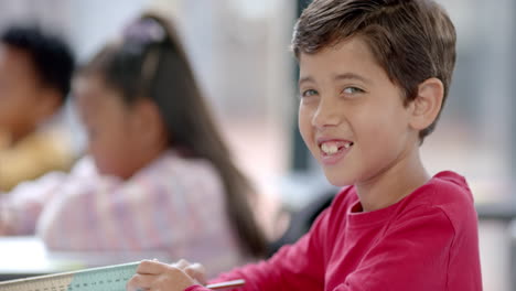 in school, boy in red shirt smiling at camera with copy space in classroom