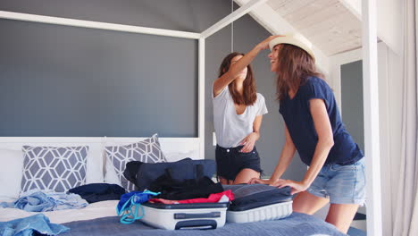 two female friends in bedroom packing suitcase for vacation