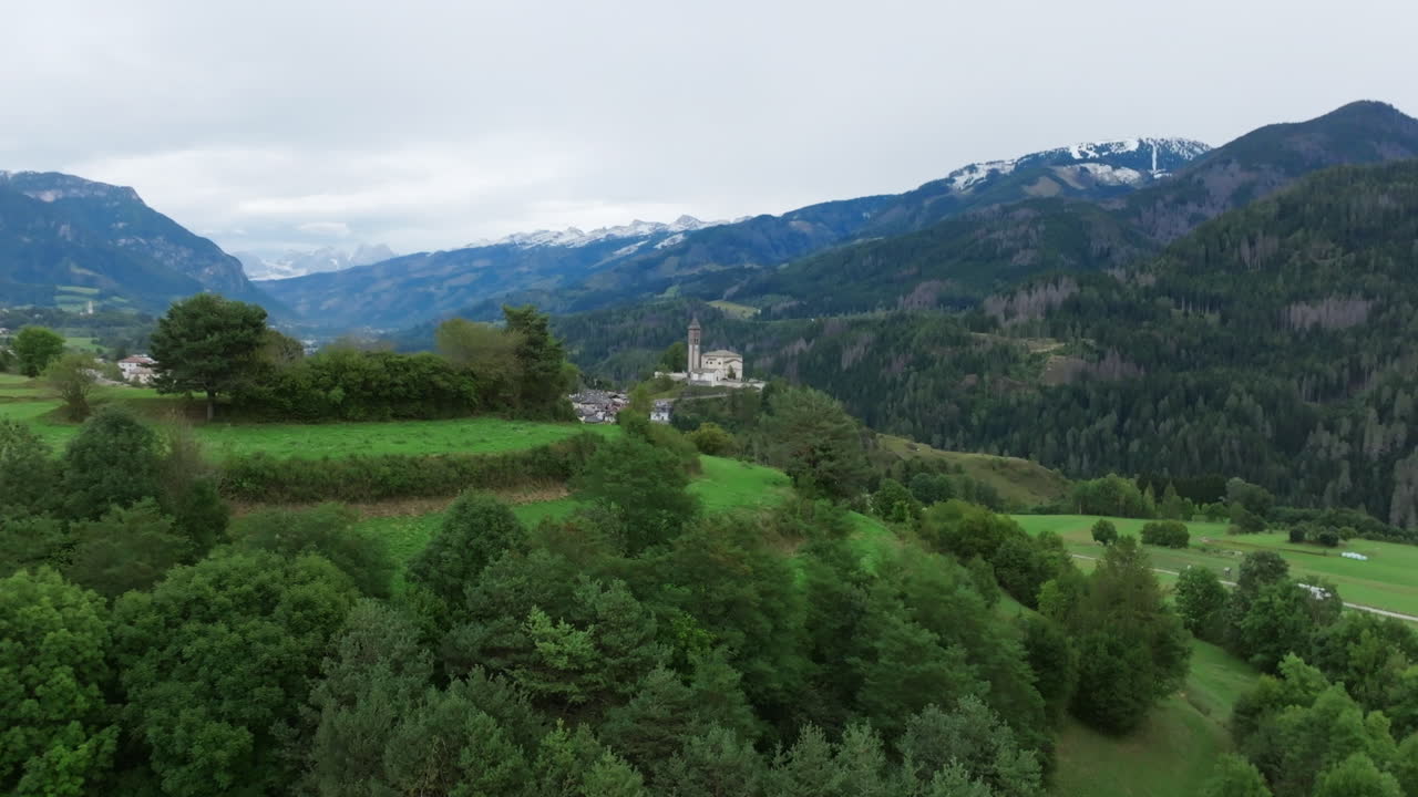 Fast aerial footage flying around a green hilltop revealing a church on a hill and a small Italian town in northern Italy.