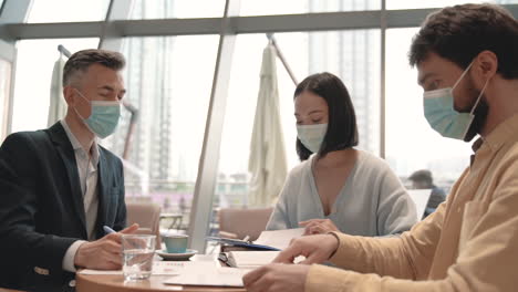 a work team with masks talks about work stuff in a coffee shop