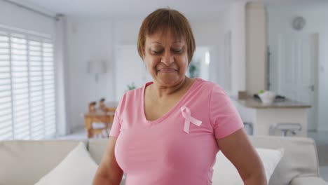 Portrait-of-smiling-african-american-senior-woman-wearing-pink-t-shirt-and-pink-breast-cancer-ribbon