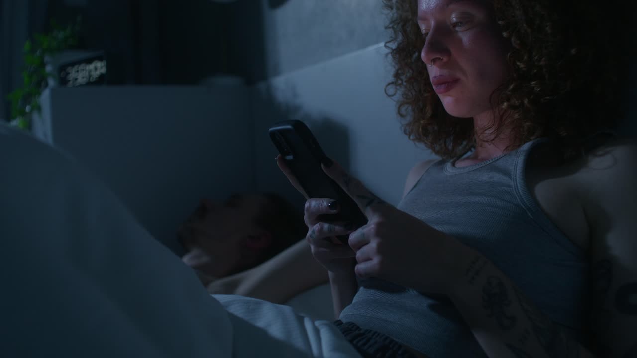 mujer enviando mensajes de texto en su teléfono inteligente en la cama por la noche