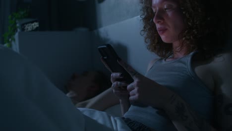 mujer enviando mensajes de texto en su teléfono inteligente en la cama por la noche