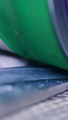 huge heavy green shaft rotating slowly over the conveyor. diaper production enterprise in blur. close up. vertical video