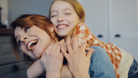 portrait of the attractive caucasian woman and her daughter hugging her from behind, mom and daughter laughing. close up. inside