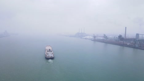 steel barge navigating foggy detroit river past zug island steel mill