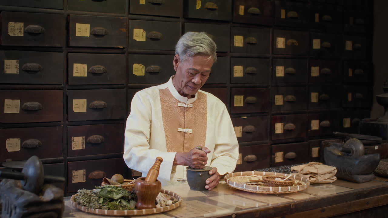 Portrait of Cheerful Senior Asian Apothecary Pounding Herbs in Mortar