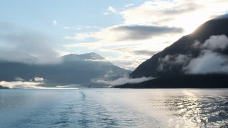 Seagulls-follow-unseen-ship-leaving-ocean-mountain-port-at-sunrise