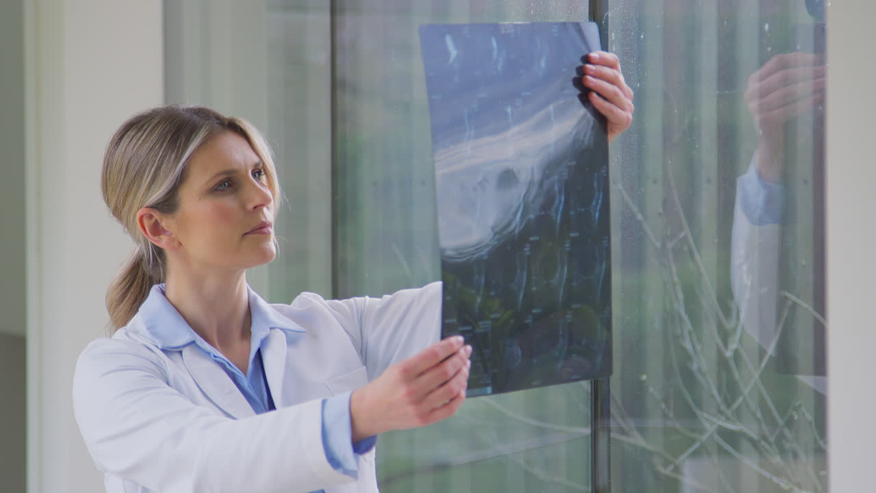 Female Doctor Wearing White Coat Standing In Hospital Corridor Looking At CT Or MRI Scan